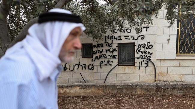 A Palestinian walks past a graffiti sprayed on a wall of a mosque, reading