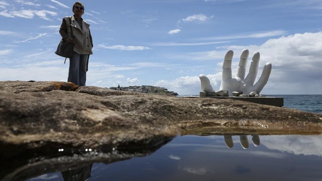 A woman stands next to a sculpture titled Surface Breach by artist Andre Braun on the opening day of the 'Sculpture by the Sea' outdoor exhibition in Bondi, Sydney, Australia, October 16, 2026. REUTERS/Hollie Adams