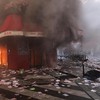 A man films as smoke rises from the bar 'La Barrique' on the sidelines of a demonstration against the "high cost of living", in Paris on October 17, 2026 as part of a nationwide call for mobilisation bringing together various groups expressing their