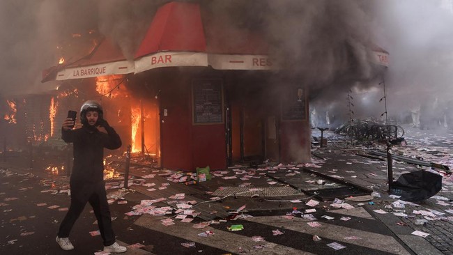 A man films as smoke rises from the bar 'La Barrique' on the sidelines of a demonstration against the 