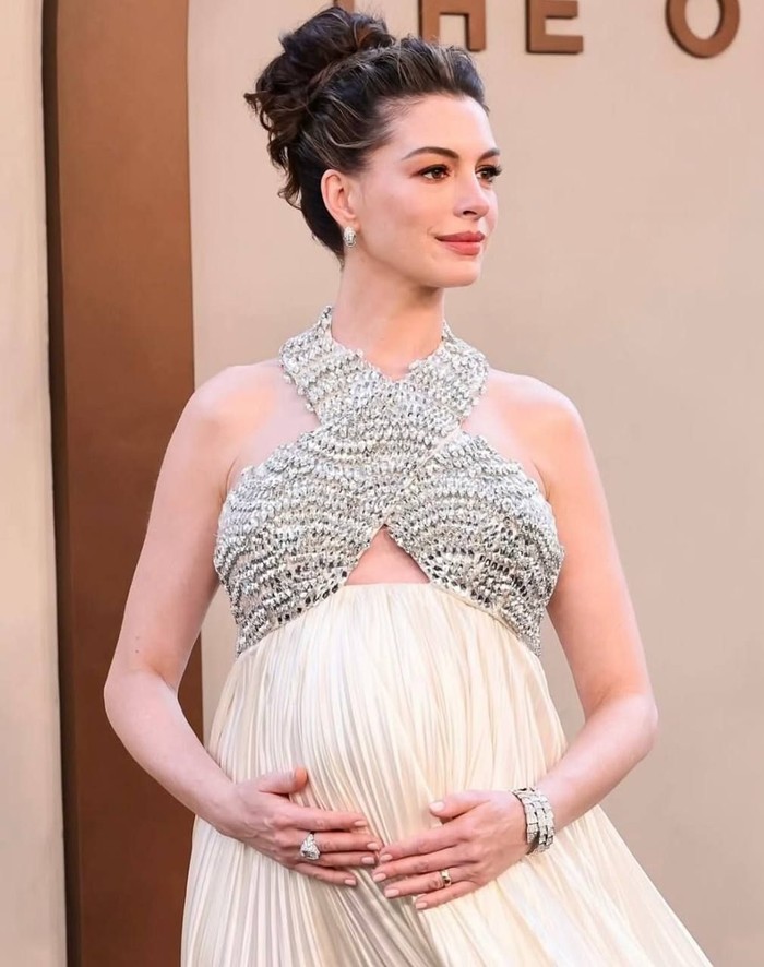 Definisi pregnancy glow, ia tampil dengan gaun berwarna ivory dengan detail halter neck potongan silang yang dihiasi embellishment silver sehingga membuatnya terlihat semakin glam/ Foto: Instagram.com/annehathaway.daily