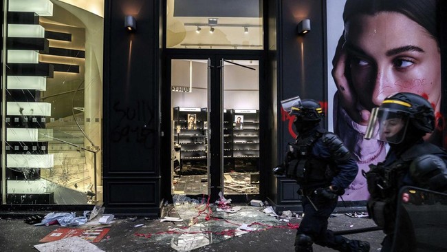 CRS riot Police officers walk past a ransacked store during ongoing protest action against the