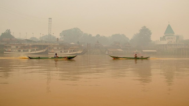 People ride wooden boats on the Kahayan River as haze from wildfires shrouds Palangka Raya, Central Kalimantan province, Indonesia, October 18, 2026. REUTERS/Arief Rahman Septian Prathama