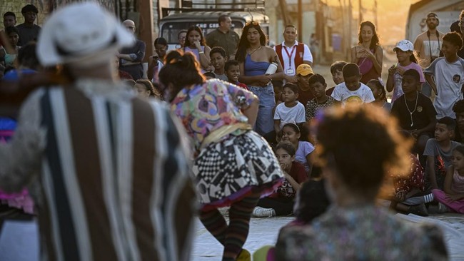 People watch a performance by members of the TET Center for Artistic Creation during the 6th Social Festival of Performing Arts in Playa Verde, Catia La Mar, La Guaira state, Venezuela, on October 18, 2026. The TET Center for Artistic Creation perfor