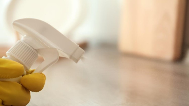 Person in gloves spraying detergent onto wooden table indoors&comma; closeup&period; Space for text