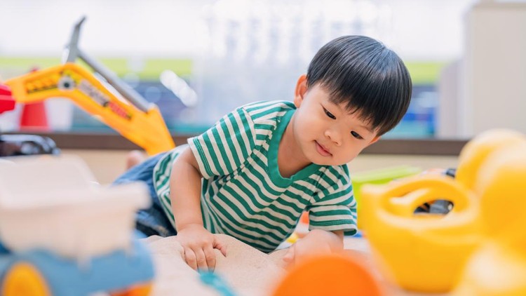 Asian boy child concentrates joyfully while playing in sandbox with colorful plastic toys and tools&comma; developing creativity and fine motor skills through imaginative exploration at indoor playground facility&period;