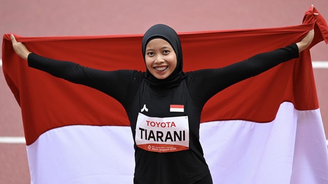 Pelari para Indonesia Karisma Evi Tiarani membentangkan bendera Merah Putih usai finis pada final 100 meter T63 Asian Para Games 2026 di Stadion Paloma Mizuho, Nagoya, Aichi, Jepang, Rabu (21/10/2026). Tiarani berhasil meraih medali emas usai finis p