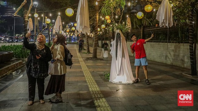 Sejumlah pejalan kaki melintasi instalasi bertema Halloween di sepanjang trotoar kawasan Sudirman, Jakarta, Rabu (21/10/2026). (CNN Indonesia/Febria Adha L)