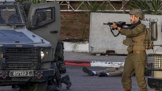 EDITORS NOTE: Graphic content / Israeli army soldiers take position next to one of the bodies of two armed Palestinian men after an exchange of fire at the northern checkpoint of Hebron, in the Israeli-occupied West Bank, on October 23, 2026. Israeli