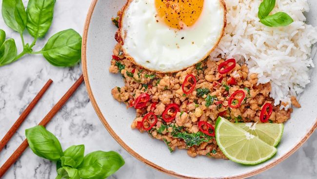 Pad Krapow Gai - Thai Basil Chicken with Rice and fried Egg on white marble background. Pad Krapow is Thai cuisine dish with minced chicken or pork meat, basil, soy and oyster sauces. Thai Food.