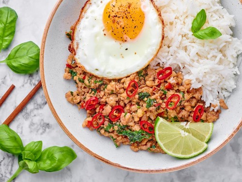 Pad Krapow Gai - Thai Basil Chicken with Rice and fried Egg on white marble background. Pad Krapow is Thai cuisine dish with minced chicken or pork meat, basil, soy and oyster sauces. Thai Food.
