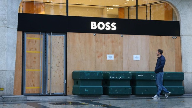 A man walks past a Boss store with its storefronts protected by wooden panels on the Champs-Elysees avenue in Paris ahead of nationwide protests called by the