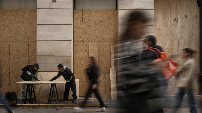 Pedestrians walk past workers cutting wooden panels to board up shops ahead of a demonstration planned for October 24, in central Bordeaux, southwestern France, on October 23, 2026. (Photo by Philippe LOPEZ / AFP)