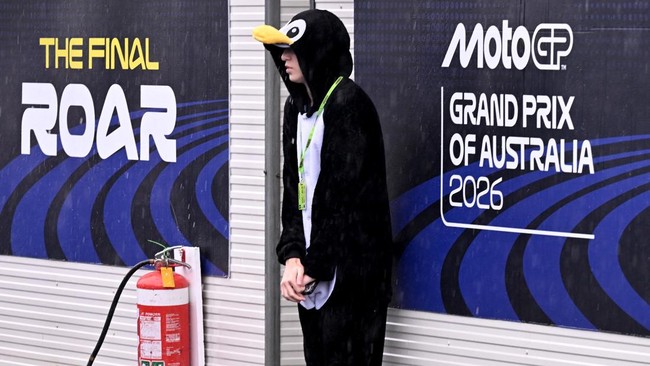 A spectator dressed in a penguin suit shelters from the heavy rain ahead at the Australian MotoGP Grand Prix on Phillip Island on October 25, 2026. (Photo by William WEST / AFP) / --IMAGE RESTRICTED TO EDITORIAL USE - STRICTLY NO COMMERCIAL USE--