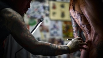 Japanese tattoo artist Horikashi, renowned for his expertise in the traditional hand-poking technique known as "Tebori," tattoos a client during a guest visit to Keith Tattoo studio in Lyon on October 20, 2026. (Photo by OLIVIER CHASSIGNOLE / AFP)