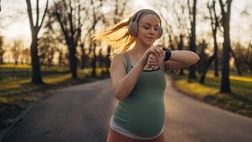 A carefree pregnant woman leads an active and healthy life during her pregnancy. She runs in the park on a sunny day and uses a smartwatch to track her workout