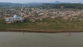 A drone view shows a man on a makeshift bamboo raft sailing through the water flowing next to the remnants of Somang village that have reemerged after the water levels in Karian reservoir, which supply water for surrounding areas including Jakarta, d