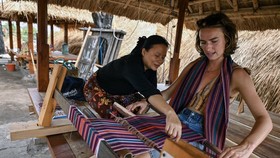 Seorang wisatawan asing belajar membuat kain tenun saat berkunjung ke Desa wisata adat Sade, Rembitan, Kecamatan Pujut, Praya, Lombok Tengah, NTB, Rabu (28/10/2026). Dua bulan pasca kebakaran yang melanda Desa wisata Adat Sade sejumlah wisatawan mula
