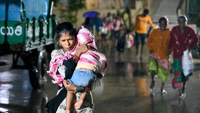A woman with a child arrives at a relief shelter during rainfall in Andhra Pradesh's Kakinada on October 27, 2026 ahead of cyclone Arnab's expected landfall. (Photo by Noah SEELAM / AFP)